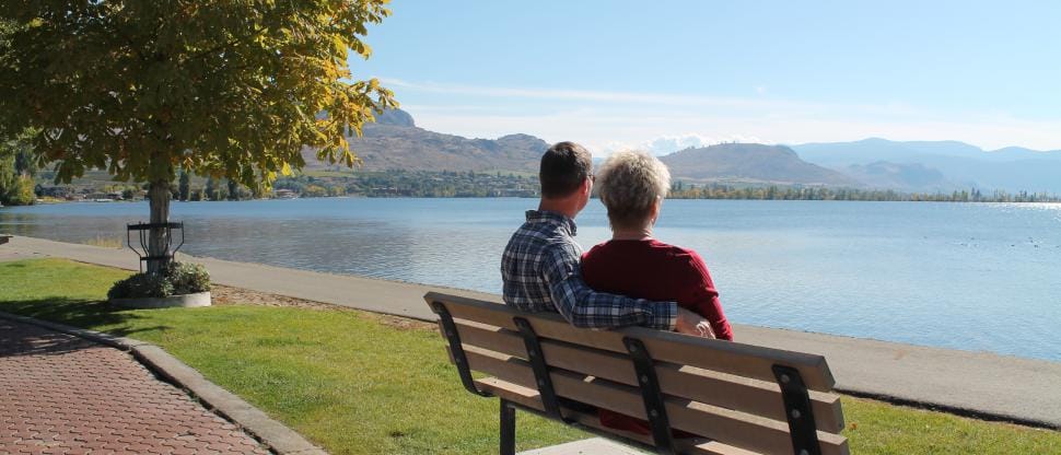 Couple sitting on park bench facing waterfront